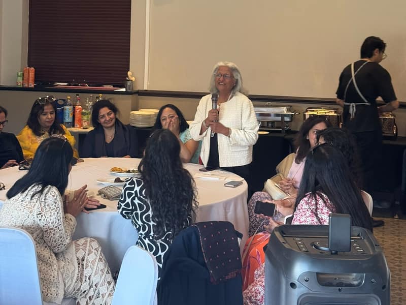 A guest speaking into a microphone as others listen around a table